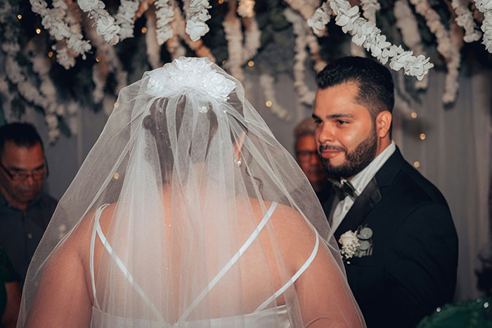 A groom in a tuxedo watches his bride, seen from behind with a veil, during a wedding ceremony. Marriage moments.