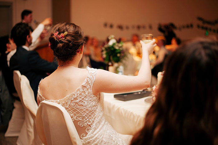 Bride in a white lace wedding dress raising a glass, celebrating a marriage moment that aged as expected.