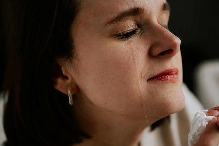 A woman crying with tears streaming down her face, holding a tissue. Illustrates expected wedding moments.