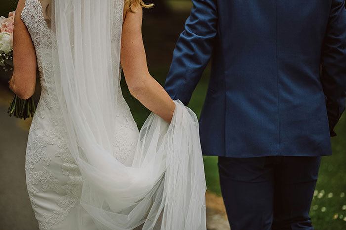 A bride in a white lace wedding dress and veil, holding a bouquet, walking arm-in-arm with a groom. Wedding moments.