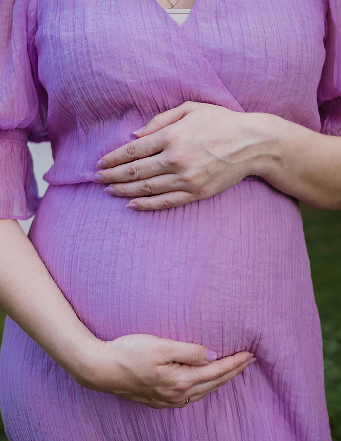 A pregnant woman in a purple dress gently holding her belly, reflecting on wedding moments that aged as expected.