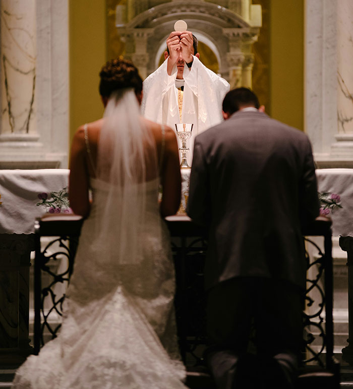 A priest performing a wedding ceremony, holding up the communion wafer, as the bride and groom kneel. Marriage moments.
