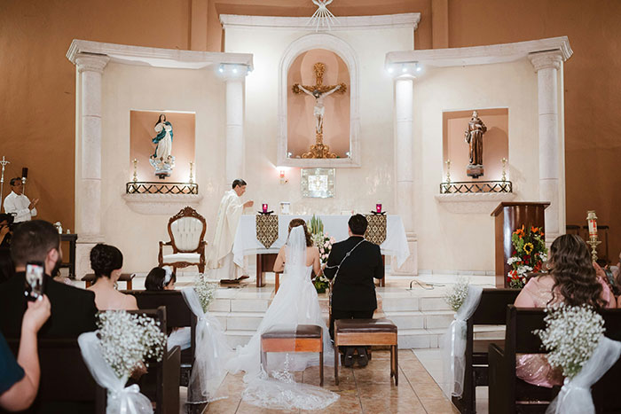 A bride and groom kneel at the altar during their wedding in a church, moments before marriage.
