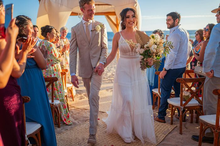 Happy bride and groom walking down aisle at beach wedding