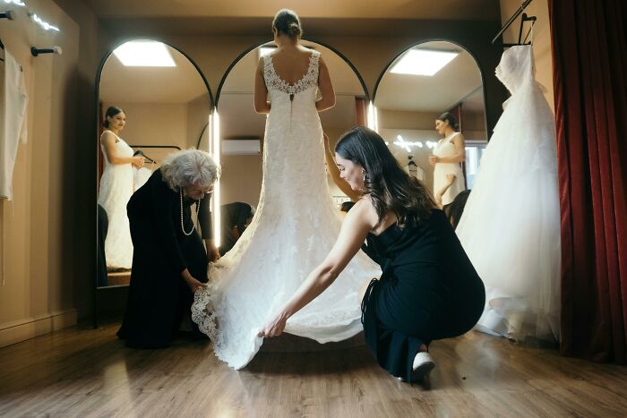 Bride trying on wedding dress with helpers adjusting train