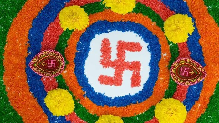 Colorful floral rangoli design with traditional swastika symbol and yellow flowers