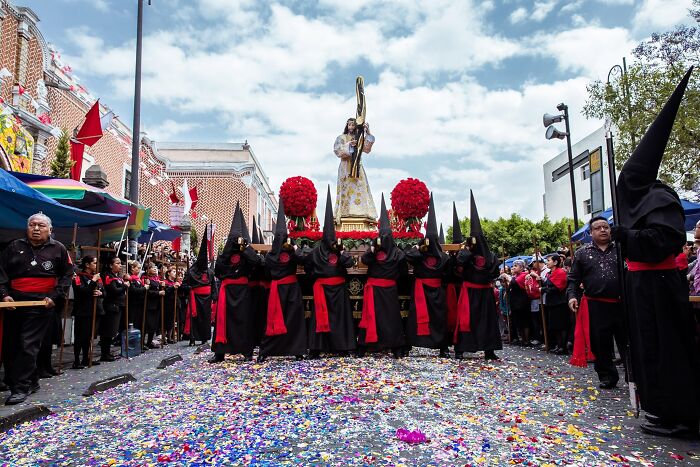 Religious procession with people in black robes and cone-shaped hoods on street