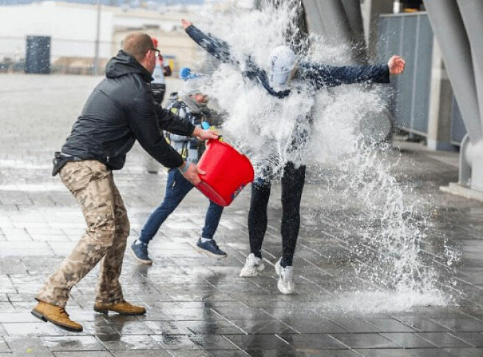 Man throwing large bucket of water on person in urban area