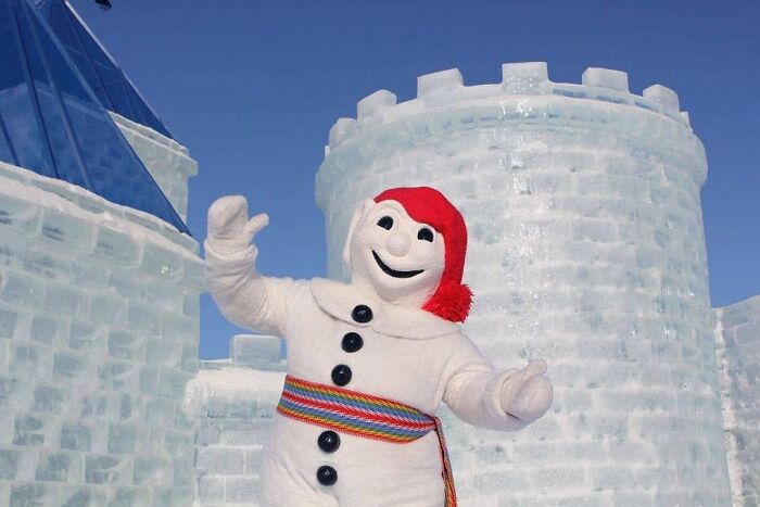 Mascot in snowman costume in front of ice castle showcasing winter festival tradition