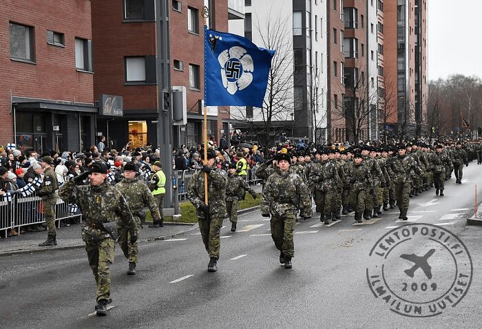 Military parade with soldiers marching and holding a blue flag