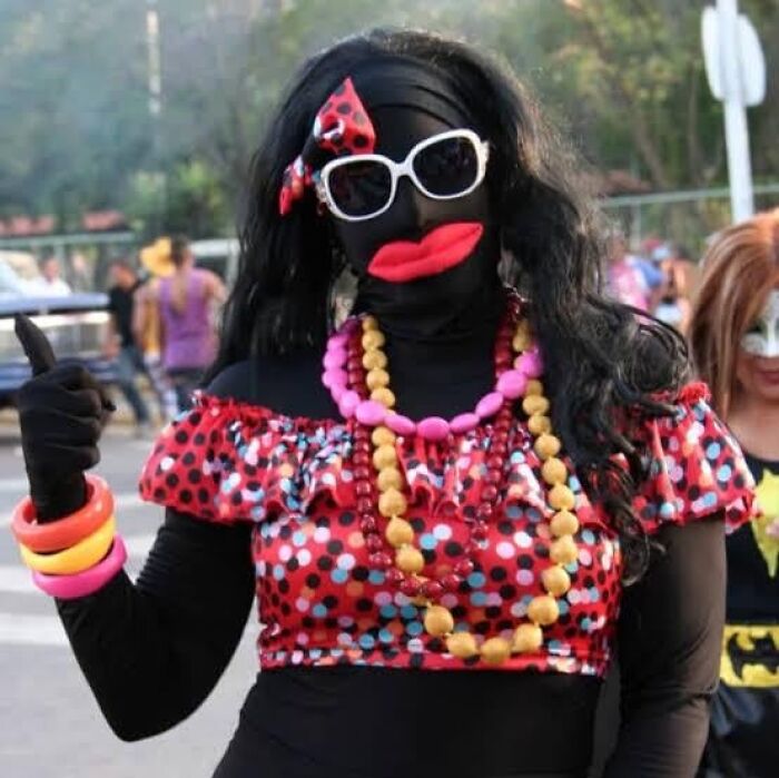 Person in blackface costume with bright accessories at local cultural event