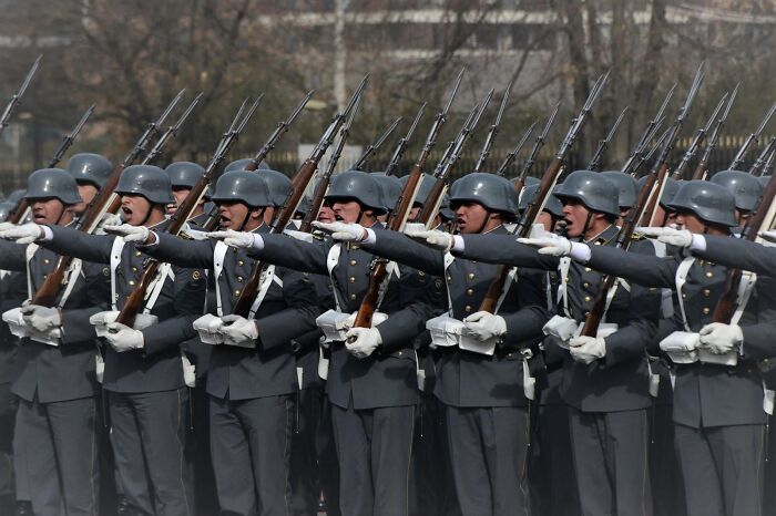 Uniformed soldiers marching in formation with rifles and helmets during parade