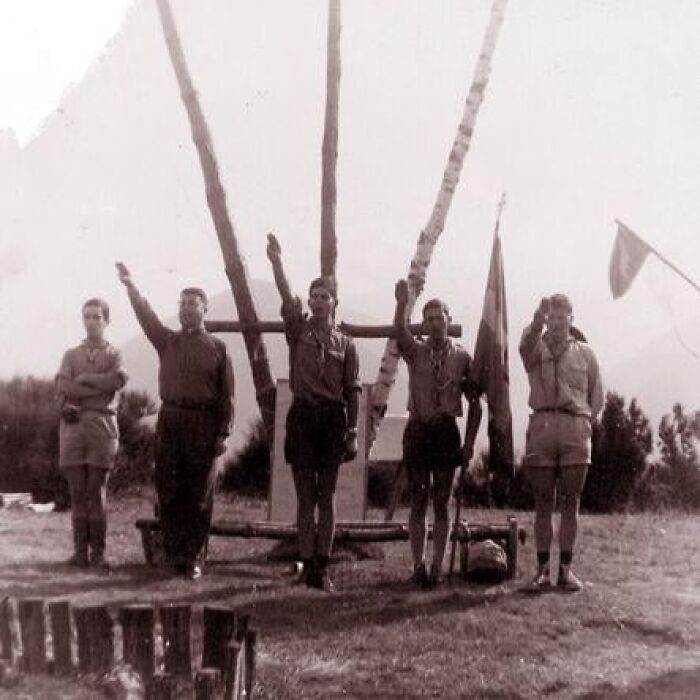 Vintage photo of boys in scout uniforms saluting outdoors