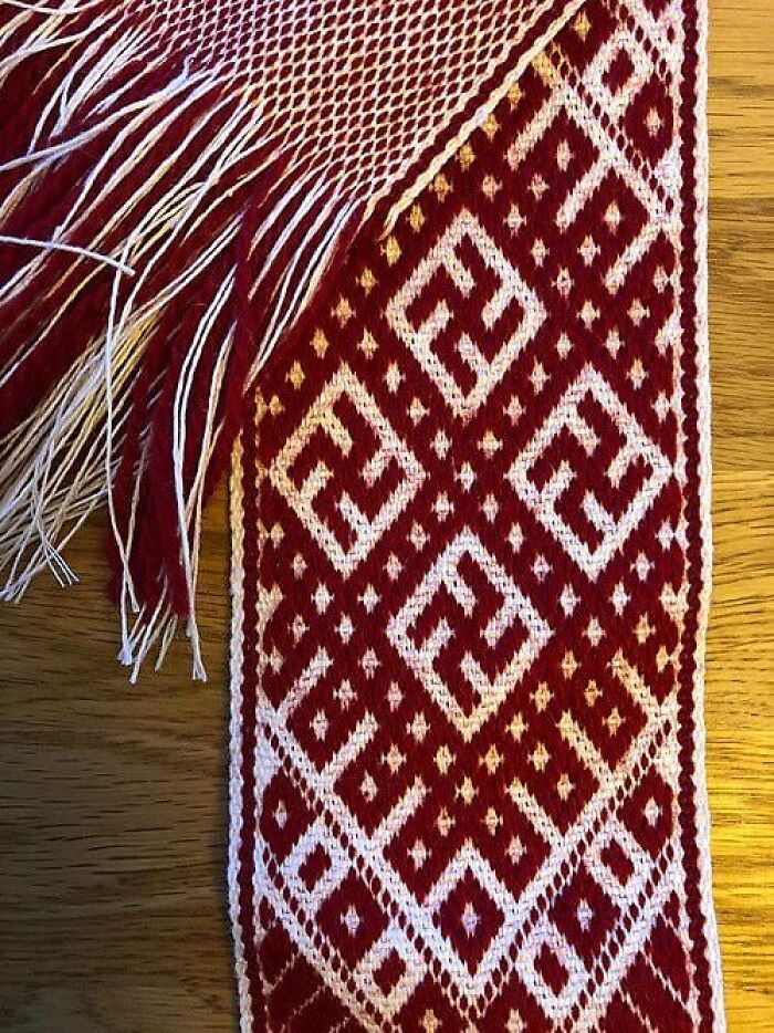 Traditional textile with red and white geometric patterns and fringes on wooden surface