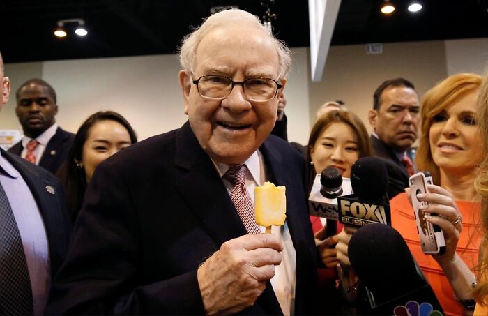 Warren Buffett smiling with ice cream surrounded by media microphones