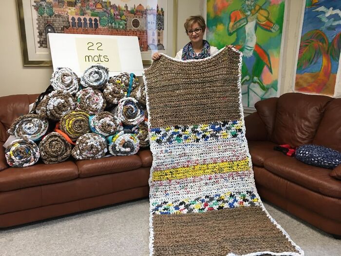 Woman holding a large homemade mat among 22 rolled mats ready to donate