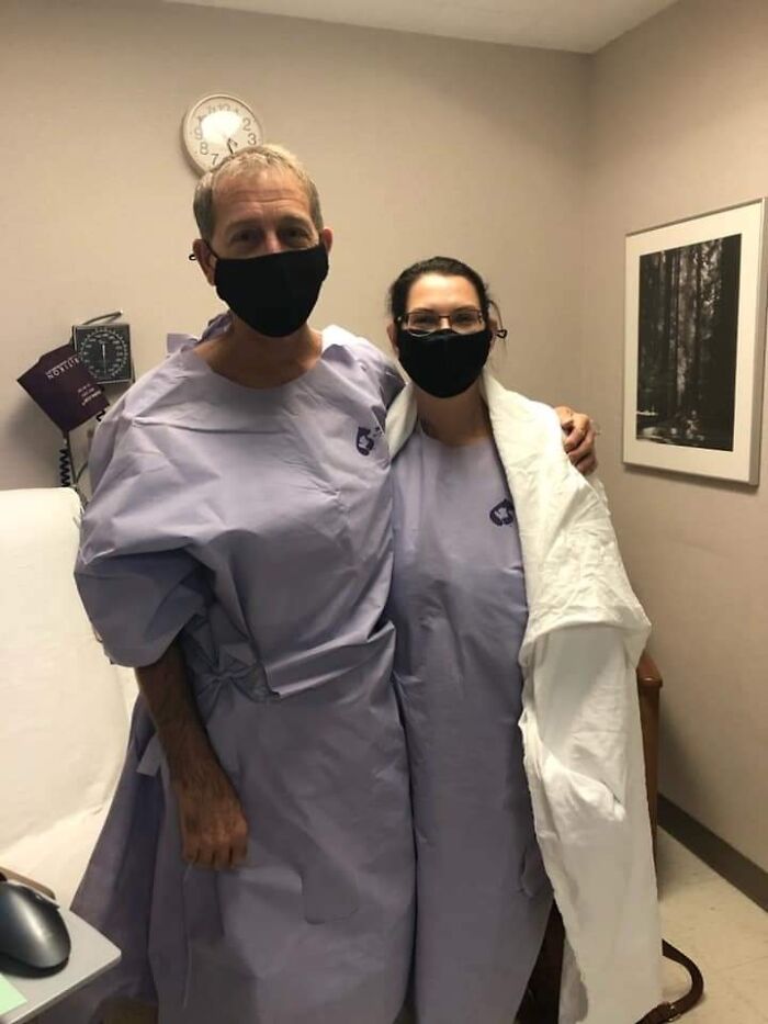 Couple in medical gowns and face masks pose supportively in clinic