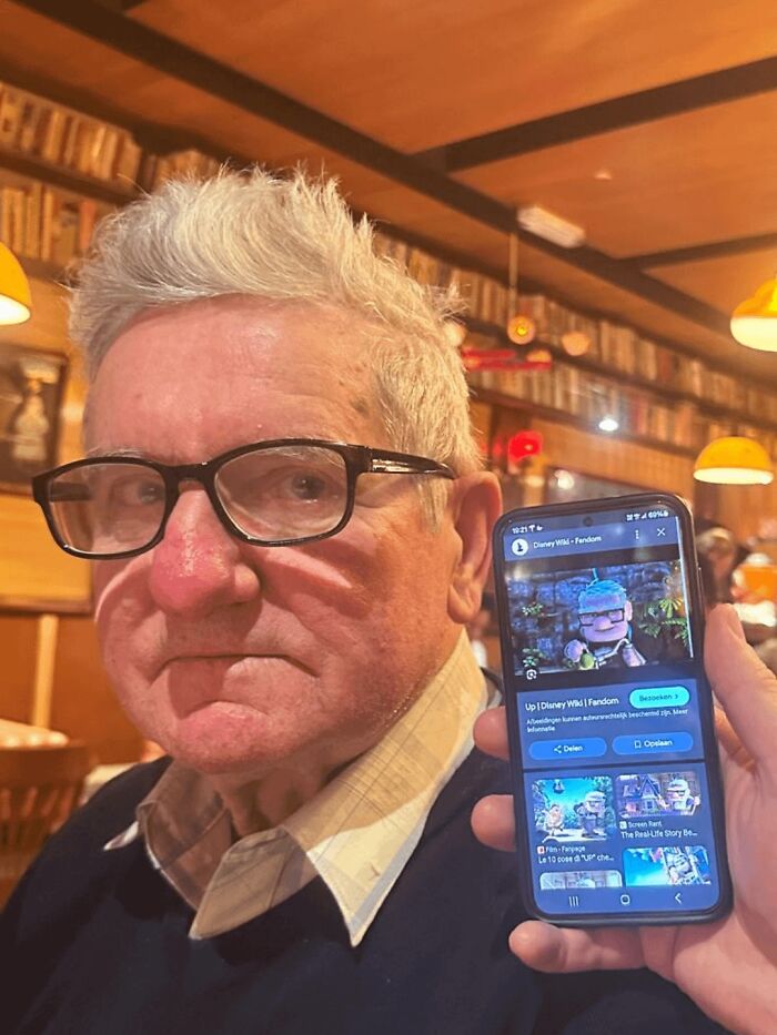 Elderly man holding phone showing a character from Disney movie Up