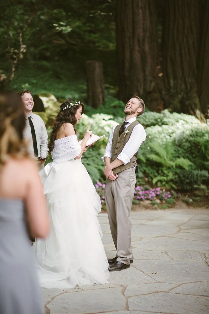 Outdoor wedding moment with bride reading vows and groom laughing