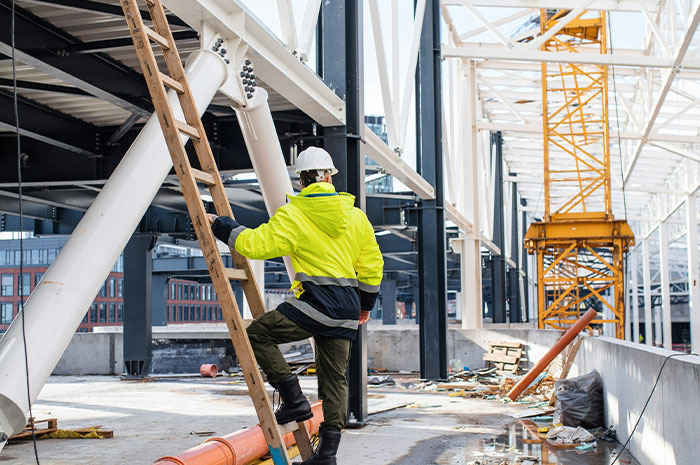 Construction worker climbing ladder at steel structure job site
