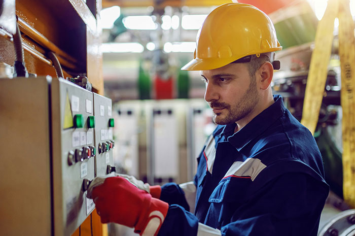 Technician adjusting control panel with safety gear in industrial career