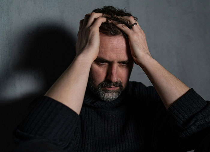 Man looking distressed holding his head, reflecting on spying on his wife and seeking a second chance