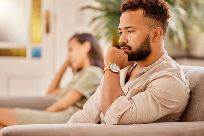 A man looking away from his wife on the couch, lost in thought. A man serving divorce papers. Postpartum wife.