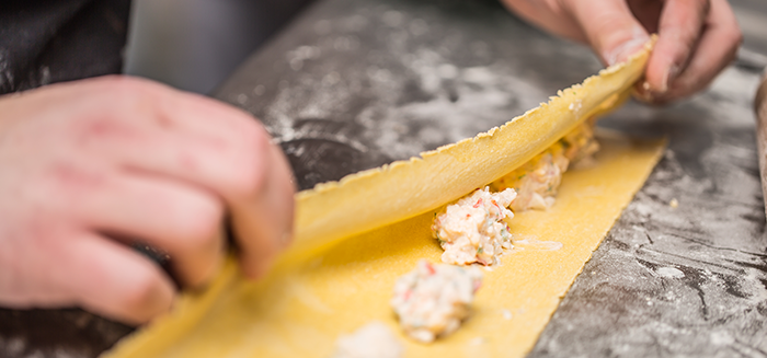 Hands folding pasta dough with filling to make homemade pasta