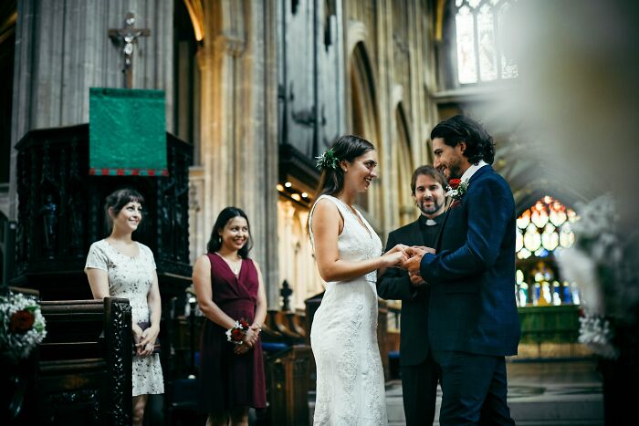 A smiling bride and groom exchanging rings during their wedding ceremony in a church, symbolizing weddings and commitment.