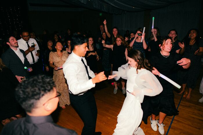 Guests dance and laugh joyfully at a wedding reception, some holding glow sticks. This scene is what happy weddings are made of.