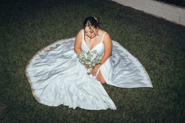 Bride in a white wedding dress sitting on grass, holding a bouquet. Showcases weddings that went off the rails.