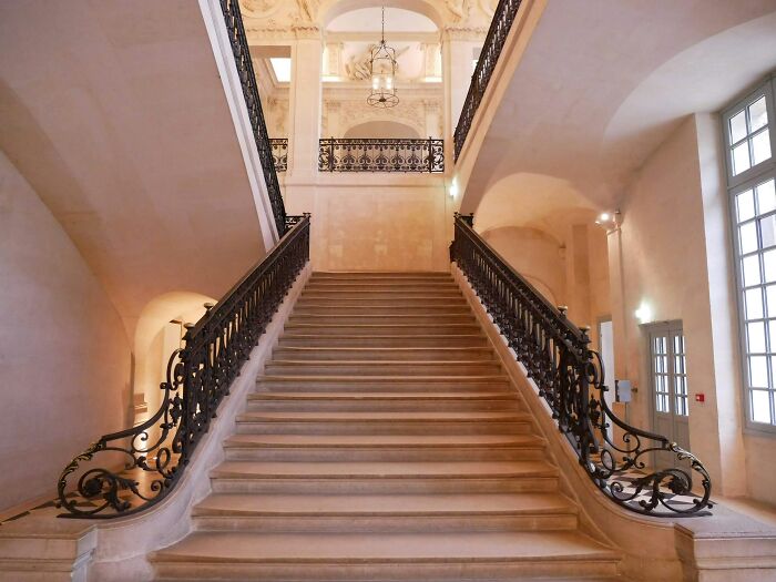 A grand, elegant stone staircase with ornate black wrought-iron railings in a building that has seen many weddings.