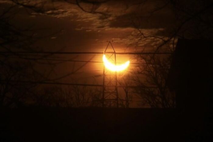 Eclipse creates rare crescent sun shape behind power line tower at night