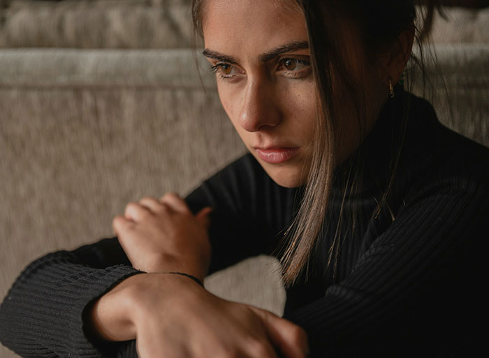 A young woman in a black turtleneck, looking contemplative, with hair falling over her shoulder, considering a dream trip.