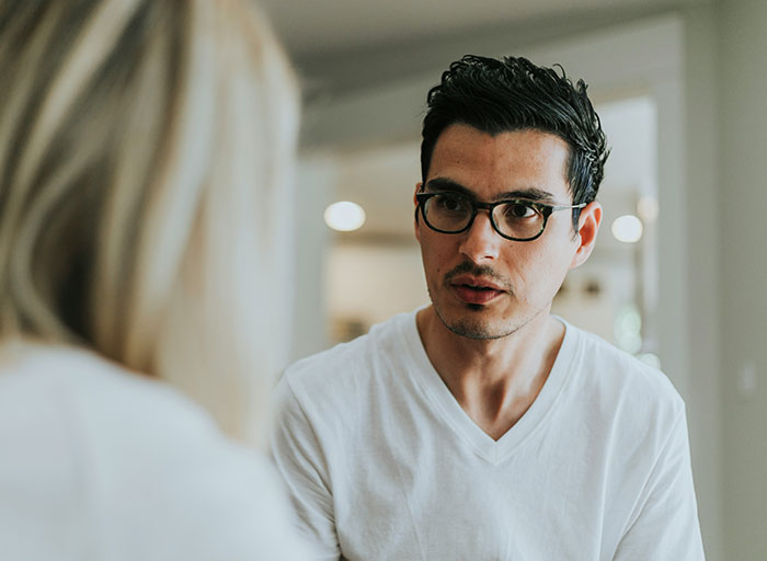 Man in glasses looks concerned, listening to a woman whose back is shown. He faces an impossible choice on a dream trip.