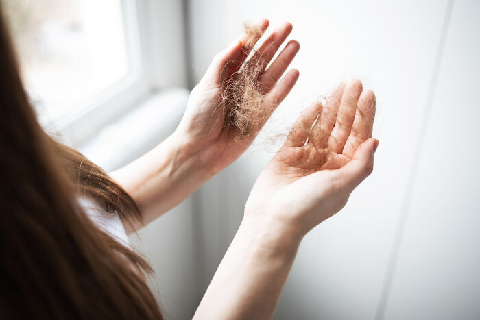 A woman's hands hold strands of fallen hair, a possible health warning sign. Discuss Routine Cancer Screening.