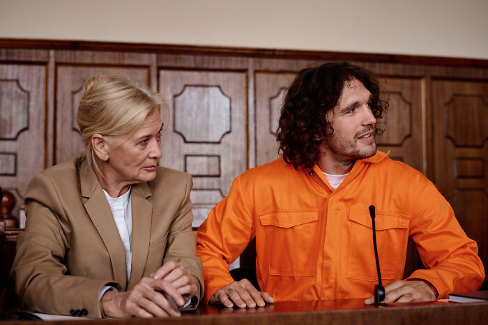 A lawyer in a beige blazer sits beside a defendant in an orange jumpsuit. This image illustrates impossible cases lawyers defend.