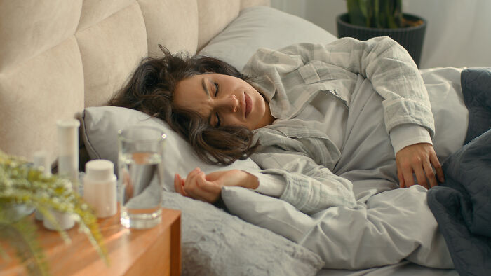 A woman in bed, visibly distressed by pain, highlights the importance of routine cancer screening for health warning signs.