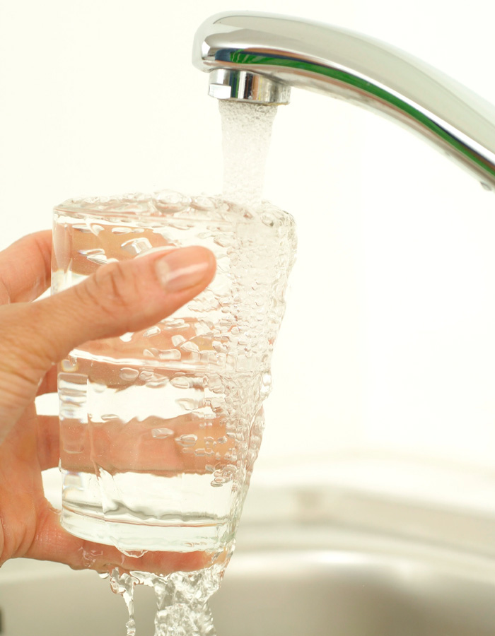 Hand holding glass under tap filling with fresh flowing tap water Hand holding glass under tap filling with fresh flowing tap water