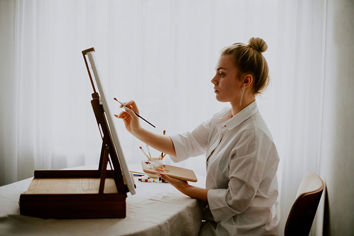 A young blonde woman painting on an easel. Her artistic pursuit may influence how young arts lovers are. A young blonde woman painting on an easel. Her artistic pursuit may influence how young arts lovers are.