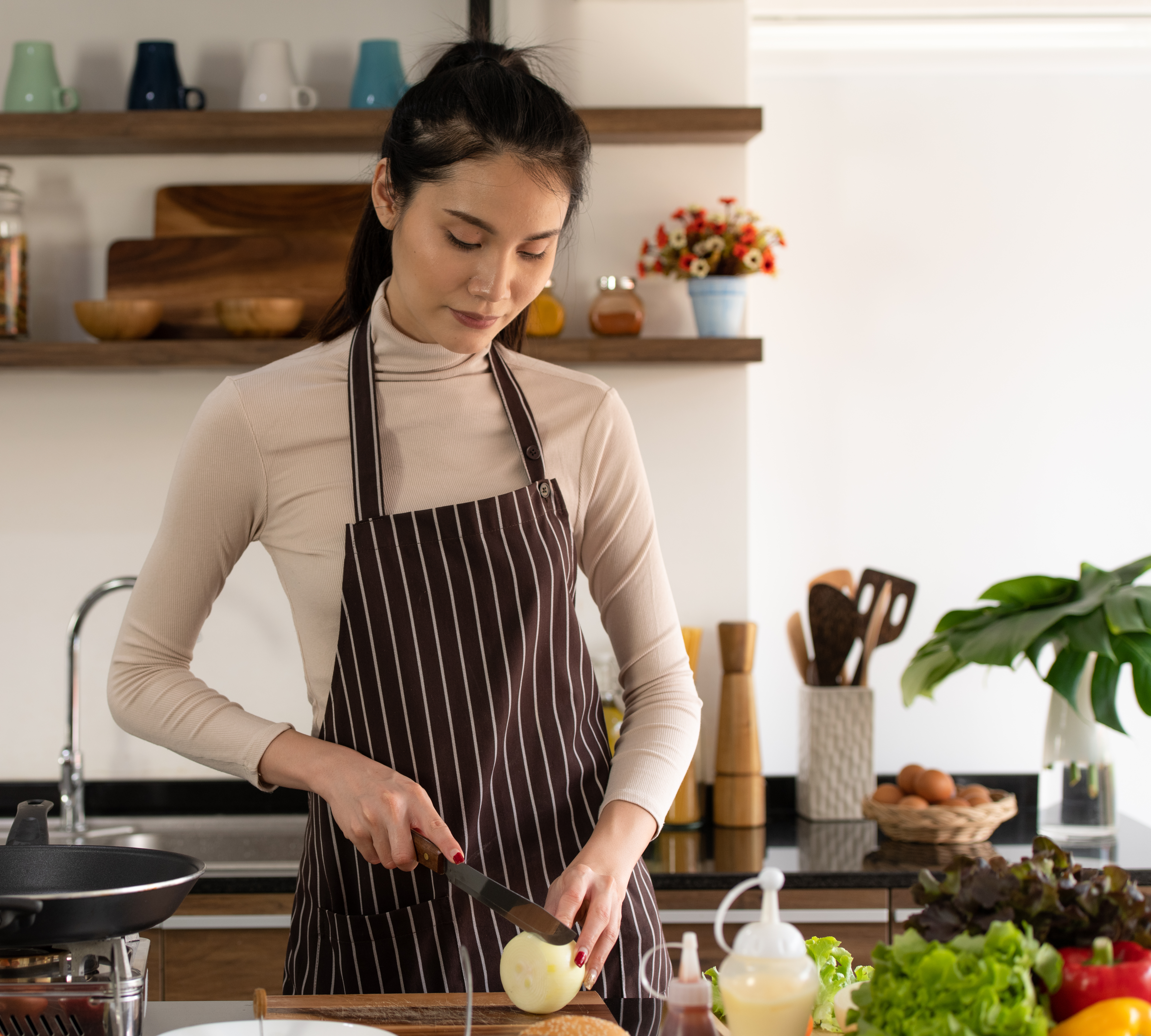 Woman wearing apron cooking in kitchen preparing food with onions