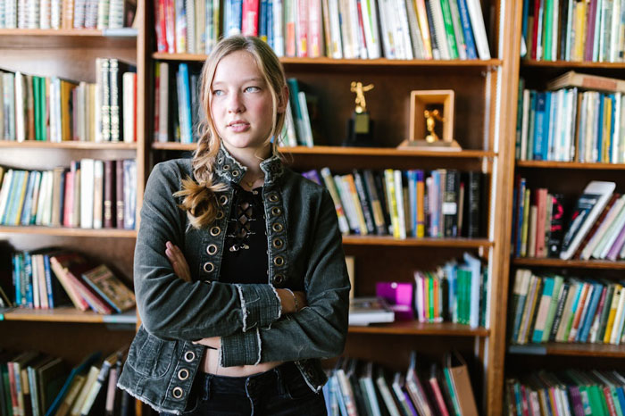 Young woman standing in front of a bookshelf showing contemplative mood relating to sister infertility Young woman standing in front of a bookshelf showing contemplative mood relating to sister infertility