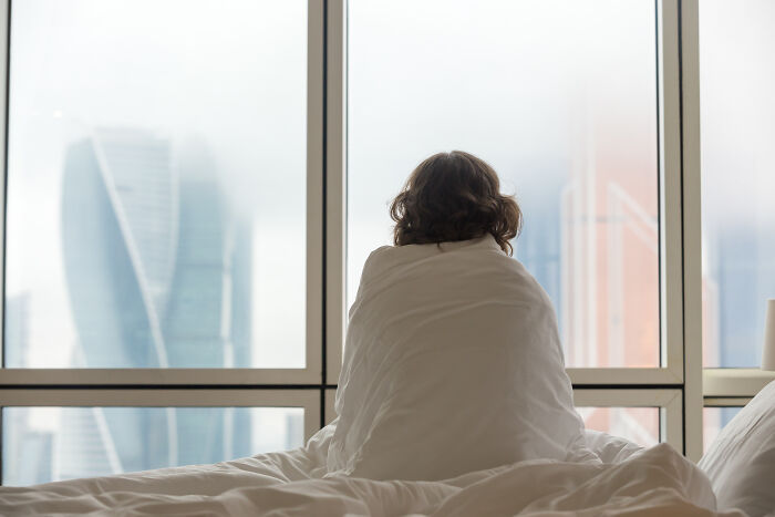 Person wrapped in blanket looking out window in psychiatric facility