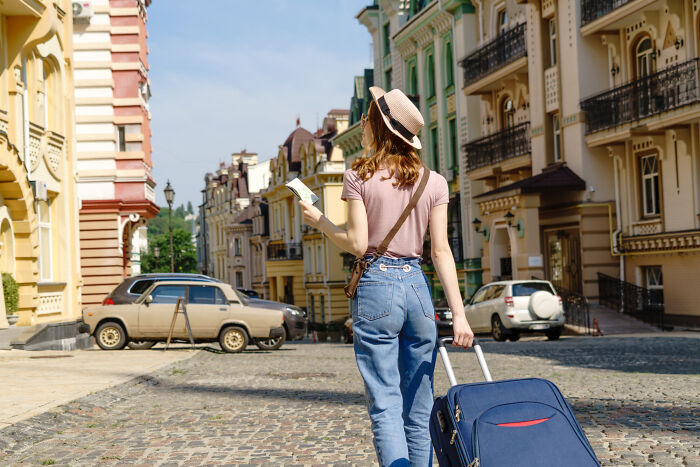 A woman with a suitcase and map walks on a cobbled street, reminiscent of moving on after heartbroken breakups.