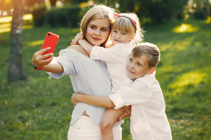 A mother takes a selfie with her two smiling children in a sunny park. It highlights a breakup's unforgettable moments.