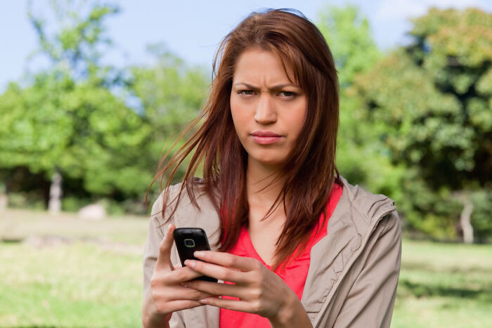 A young woman looking heartbroken, frowning at her phone in a park, reflecting on messy breakups.