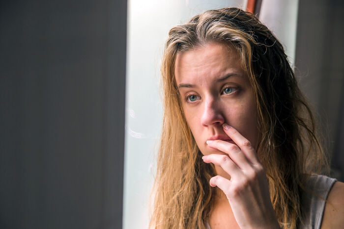 A young woman looking sad, her hand near her mouth, contemplating a messy breakup. She appears heartbroken.