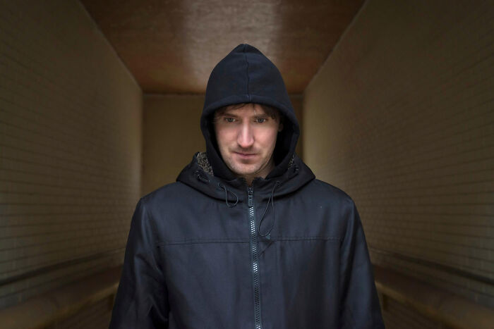 A man in a dark hooded jacket looks down, standing in a hallway, symbolizing heartbroken people and their unforgettable breakups.