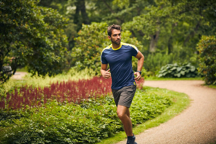 A man runs on a path through a lush green park with red flowers. He's exercising after a painful breakup.