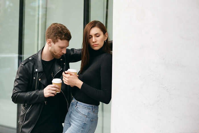 A couple with sad expressions, holding coffee cups, representing heartbroken people and messy breakups.